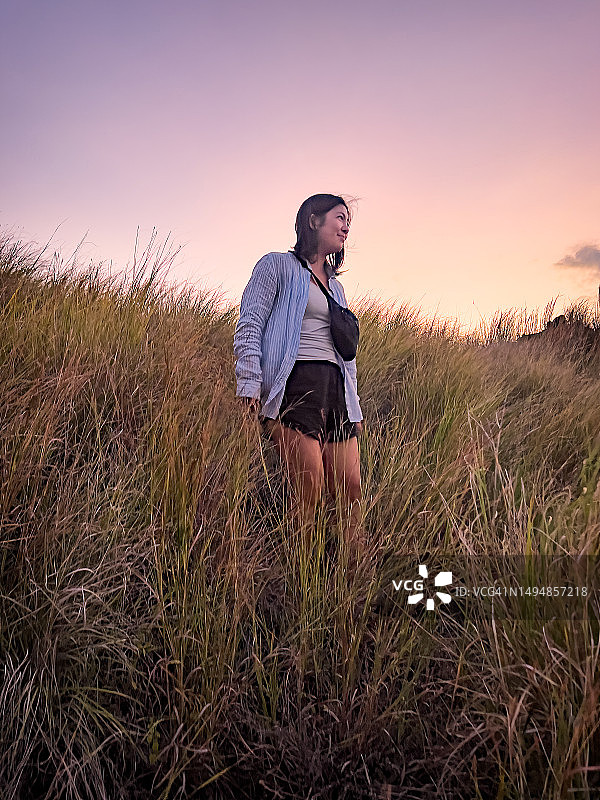 在日落时分穿过高草下坡远足的不同种族的年轻女子图片素材