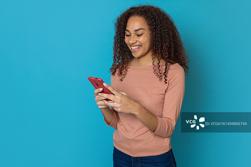 千禧一代少女拿着手机在蓝色背景前，留有复制空间。技术、社交媒体和青年生活方式概念。图片素材