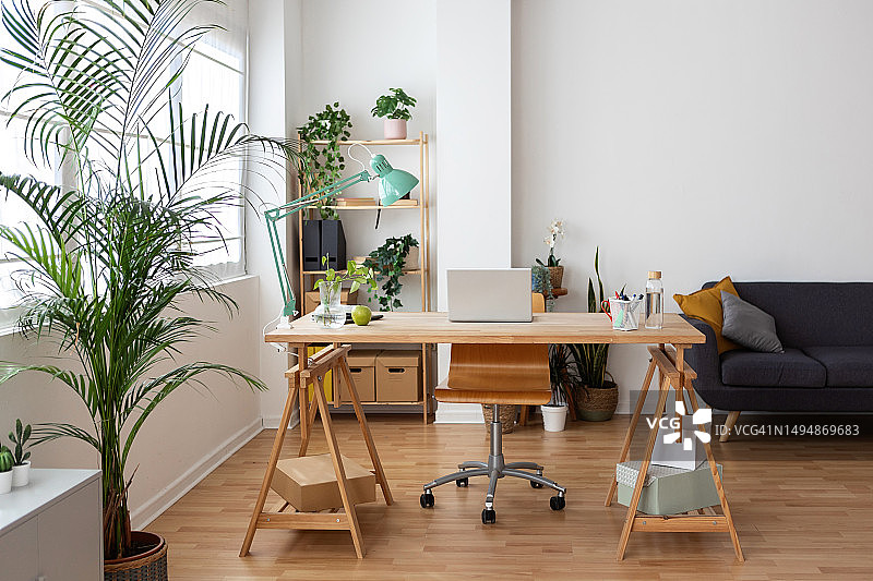 明亮现代的家庭办公室内部，木桌上放着笔记本电脑。图片素材