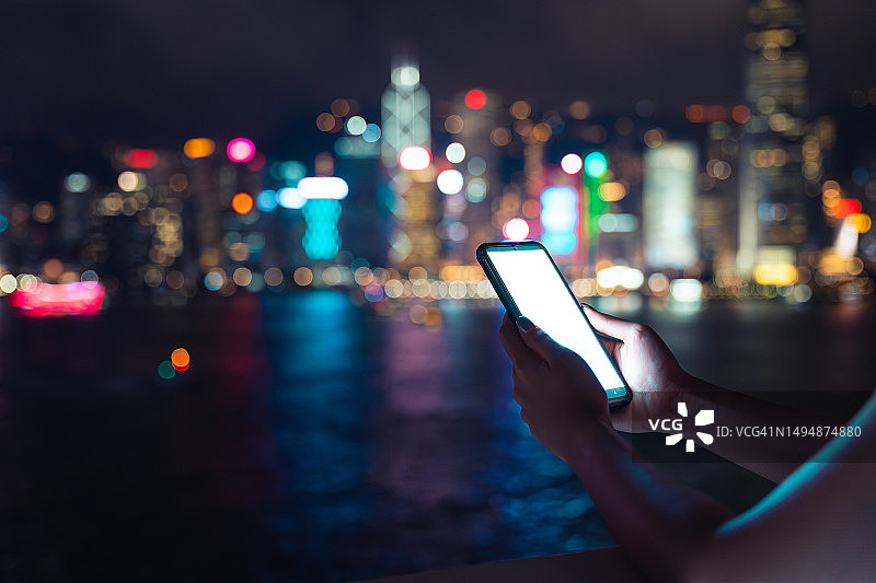 一名女子在香港的城市夜景中使用智能手机图片素材