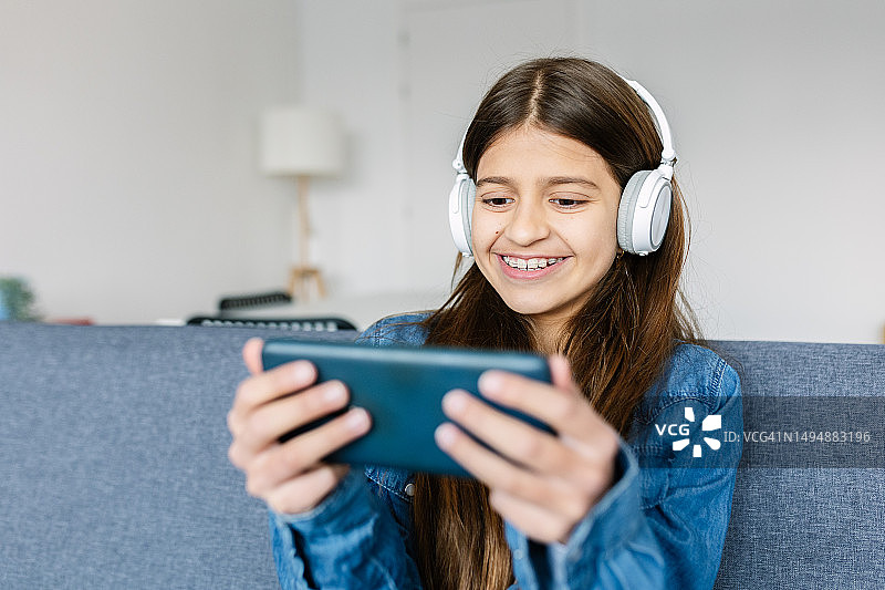 混血女孩在家里的沙发上玩智能手机视频游戏，享受乐趣图片素材