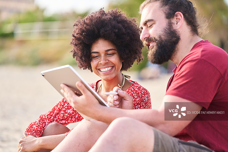 沙滩上，平板电脑男子身旁的女子图片素材