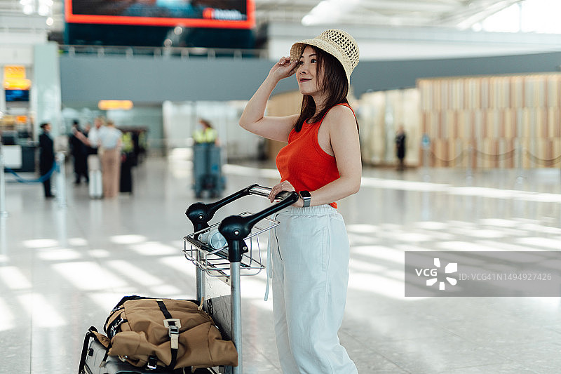 年轻的亚洲女性在机场航站楼推着行李车前往办理登机手续，旅行度假概念图片素材