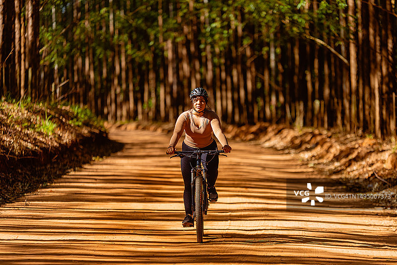 年轻女人在树林小路上骑自行车休闲健身图片素材