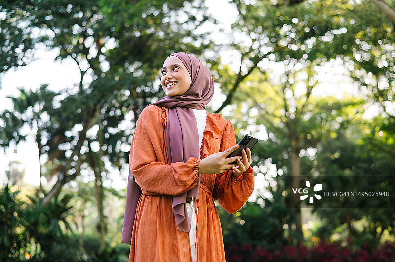 在公园里拿着手机的亚洲马来西亚女性图片素材