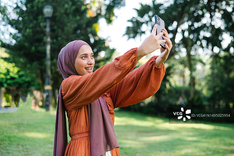 在公园里拿着手机的亚洲马来西亚女性图片素材