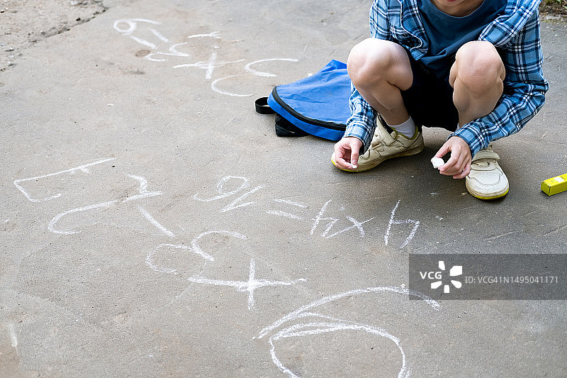 男孩在街上用粉笔写乘法例题图片素材