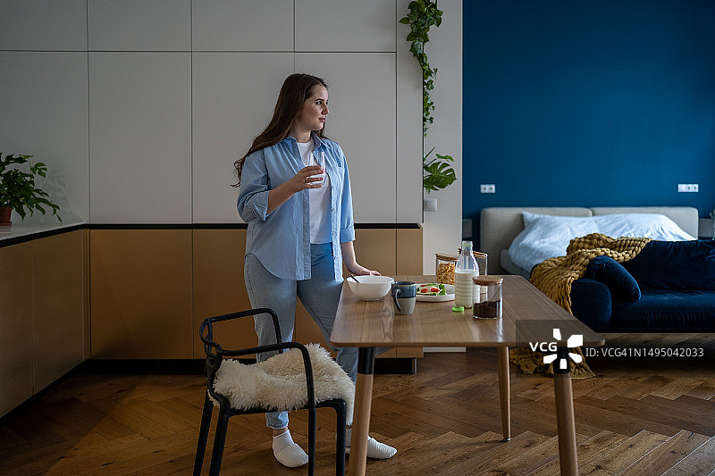 女人在现代公寓的厨房餐桌旁喝水图片素材