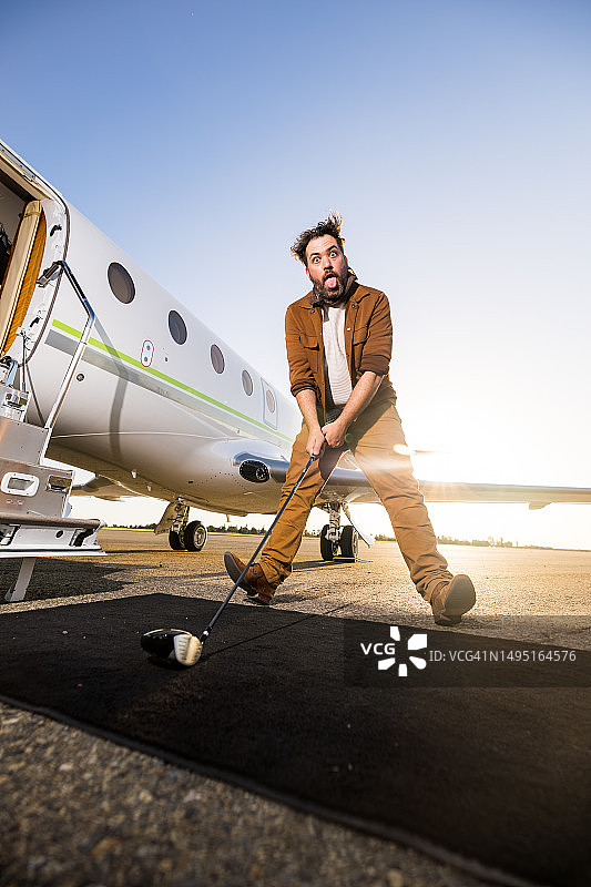 手持高尔夫球杆在私人飞机前做鬼脸的男人图片素材