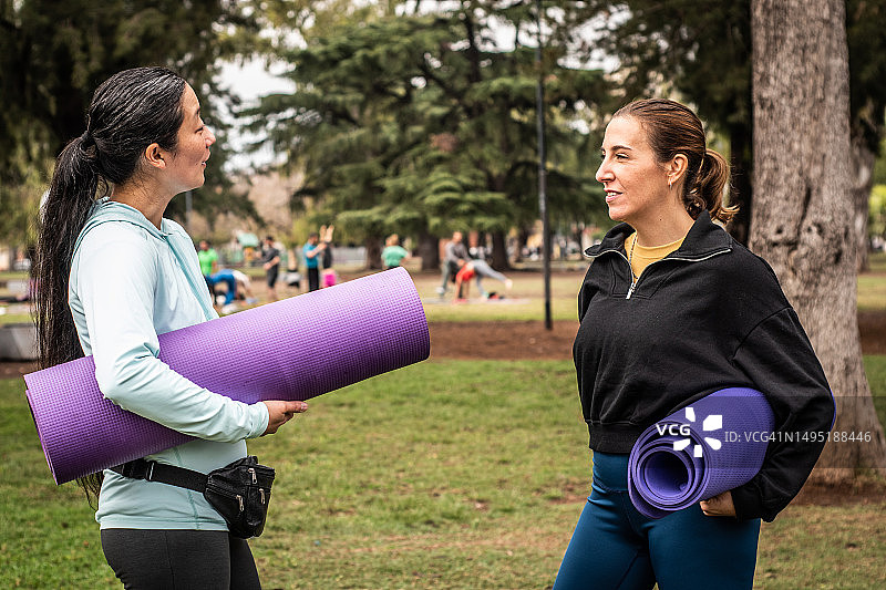 在公园拿着瑜伽垫聊天的女性朋友图片素材