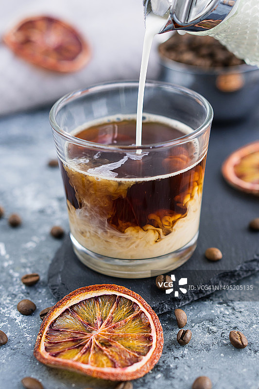 牛奶冰咖啡，夏季饮品，灰色背景冰块咖啡中倒入牛奶图片素材