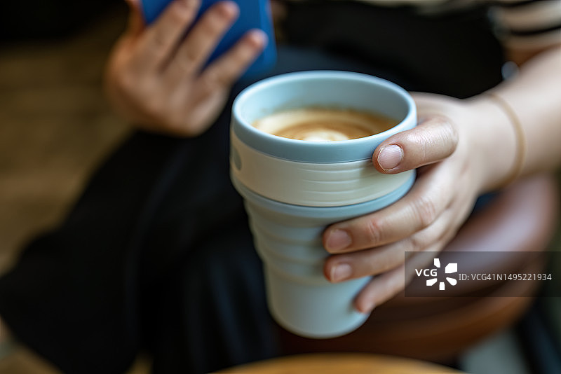 一位女士拿着一杯装在可重复使用杯子里的咖啡图片素材