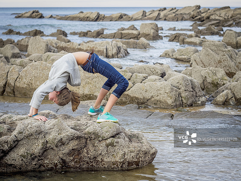在海滩岩石上后空翻的女孩图片素材