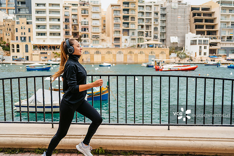 在马耳他圣朱利安长廊跑步时听音乐的年轻女人图片素材
