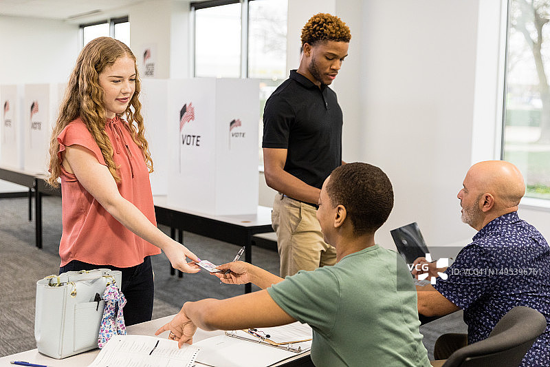 年轻女人在投票站向女志愿者出示身份证图片素材