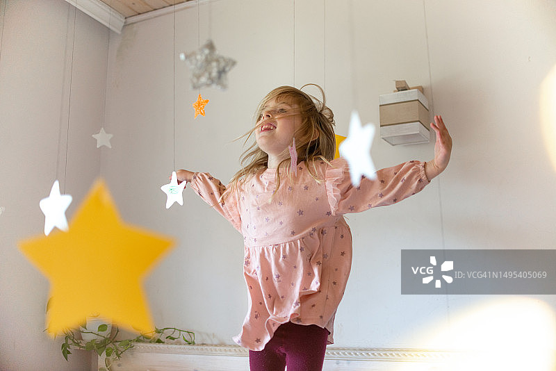 快乐的女孩在纸星星的风景中跳跃玩耍，童年幻想图片素材