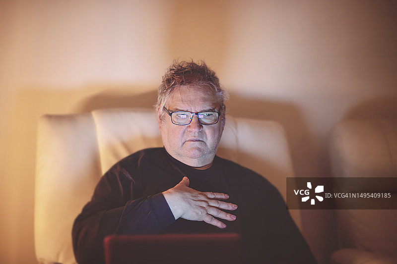 一位退休老人的休闲肖像，坐着拿着笔记本电脑，感觉不适图片素材