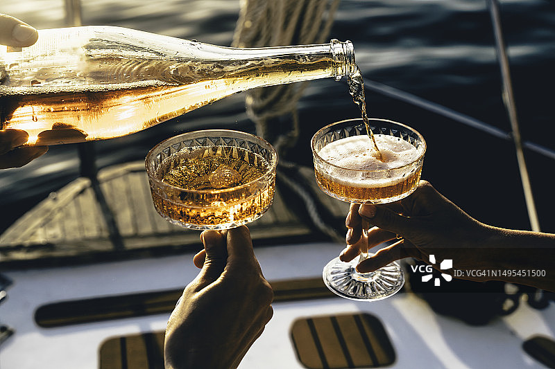 特写镜头：朋友们在游艇上日落时分碰杯起泡酒图片素材