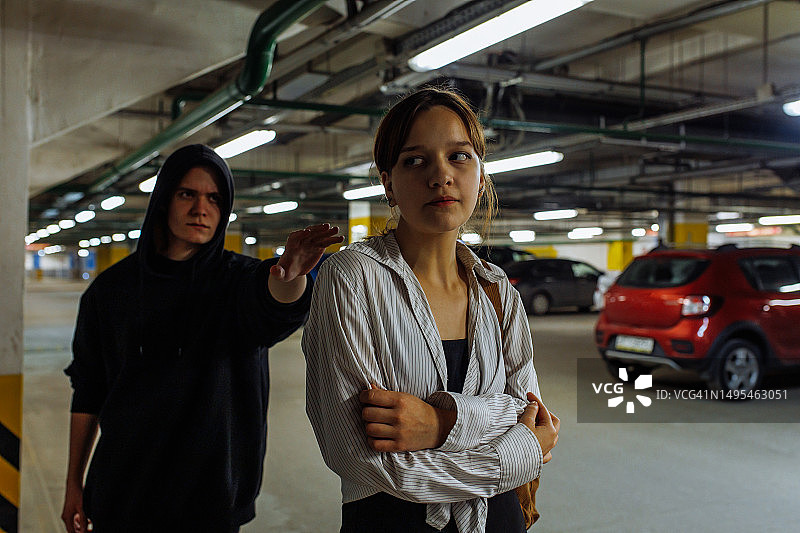 在地下停车场，一个穿黑色连帽衫的阴沉年轻人跟踪一个年轻女子图片素材