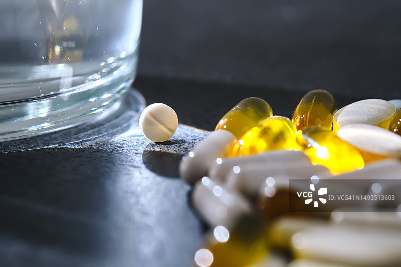 深色桌子上玻璃杯旁边的药片、维生素和膳食补充剂图片素材