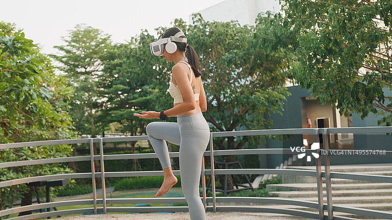 在城市公园户外练习瑜伽的亚洲年轻运动女性，戴着VR眼镜，穿着运动上衣和紧身裤。健康饮食和减肥。图片素材