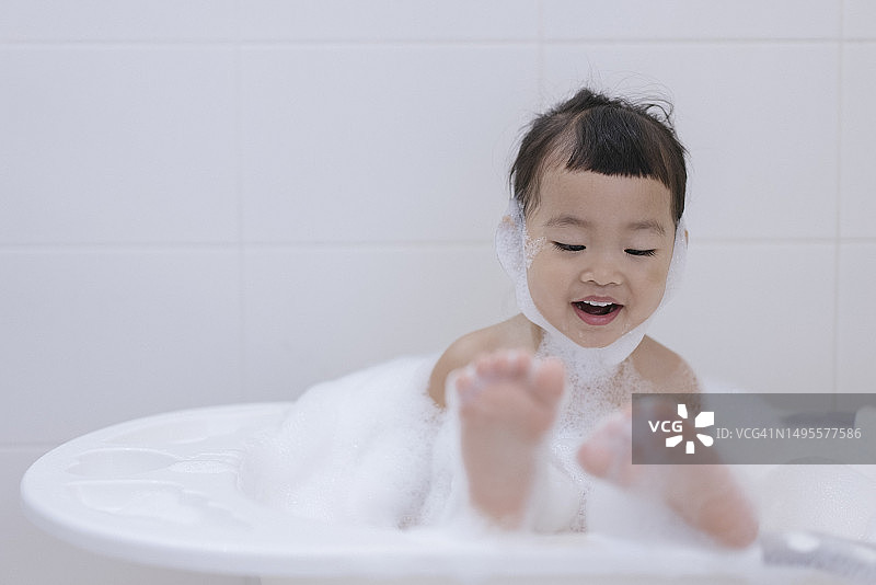 亚洲女婴在浴缸里享受清洁和泡沫，留白图片素材