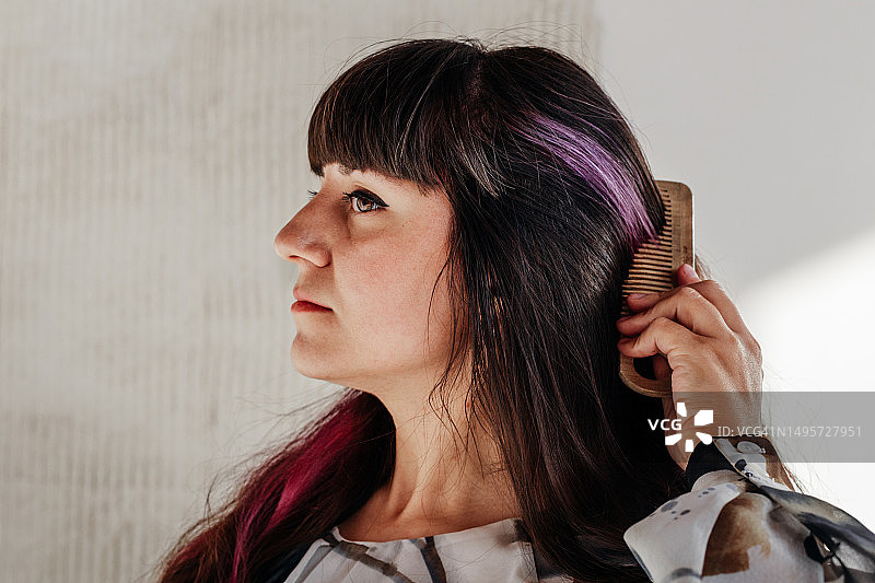 美丽的 brunette 梳理她美丽的黑色波浪头发的特写。迷人的年轻女人做她的发型。隐藏的紫色高光。文案空间。图片素材