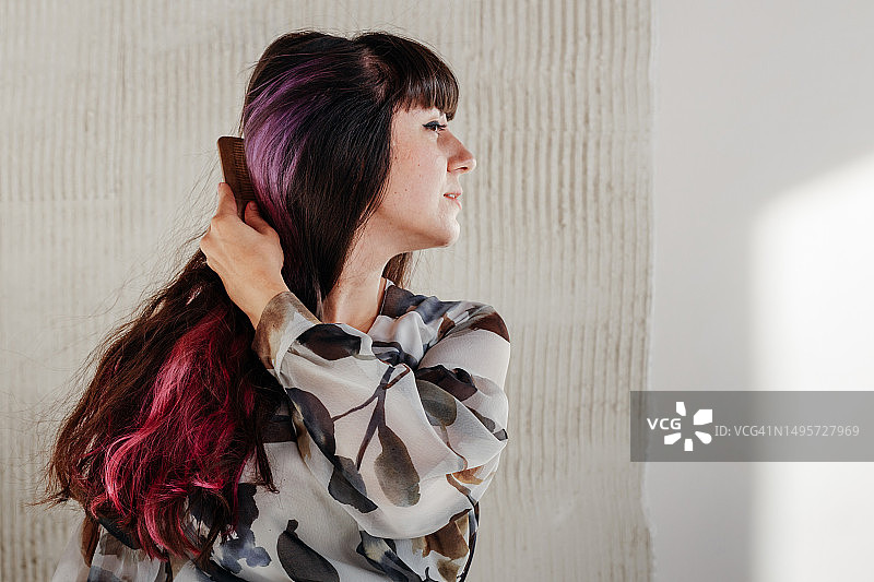 美丽的黑发女孩闭着眼睛，用木梳梳理她那闪亮的头发。黑色头发，带有隐藏的紫色挑染。留白图片素材