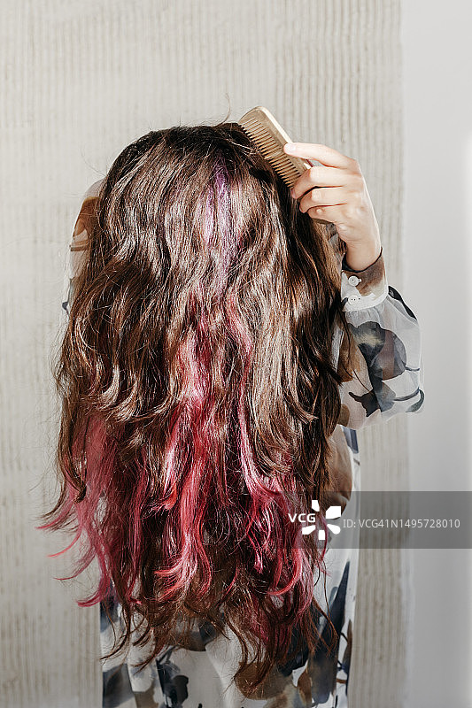 隐藏着高光和彩色发缕的美丽健康的波浪发。穿着浅色丝绸连衣裙的年轻女孩在阳光下梳理她闪亮的黑发。图片素材