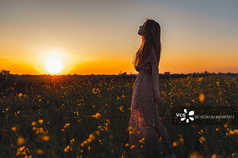 深呼吸：年轻女人在开满黄色鲜花的田野里深呼吸图片素材