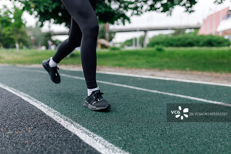 一位穿着黑色运动服的女子在户外运动场跑步图片素材