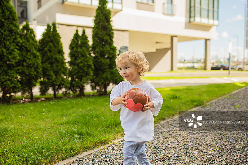 男孩在院子里玩球，夏季背景下的现代城市生活图片素材