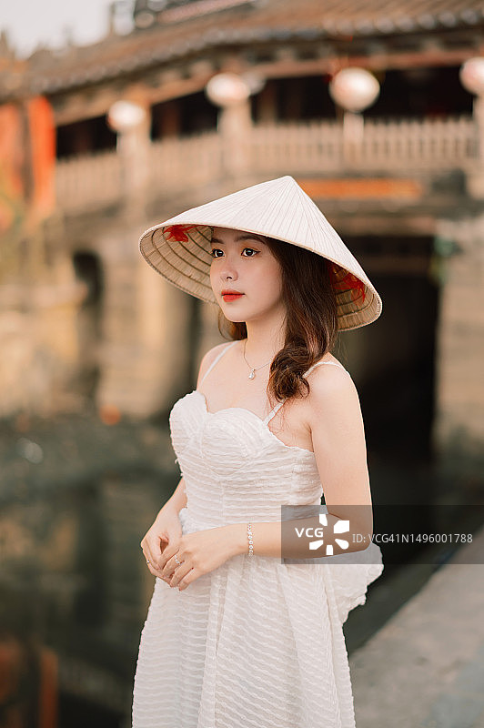 越南：戴着树叶帽子的当地女孩站在桥前图片素材