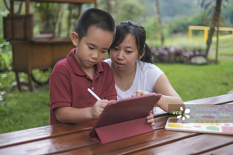 中国母亲用平板电脑辅导儿子做学前作业图片素材