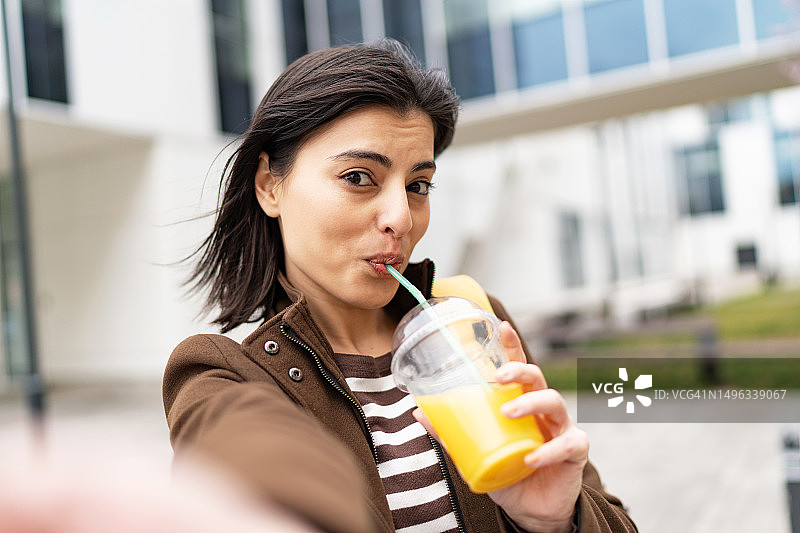 年轻女人在街上边走边自拍，手拿冰沙图片素材