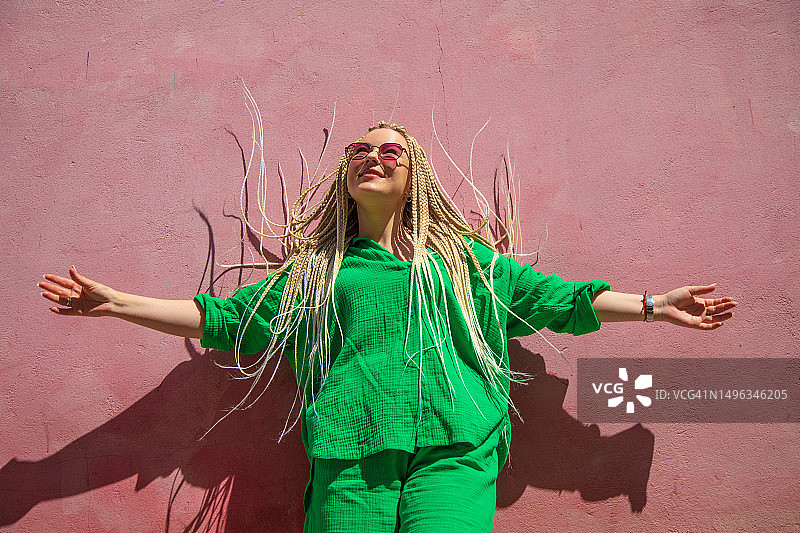 站在粉红色墙前，留着金色长辫子的漂亮女人图片素材