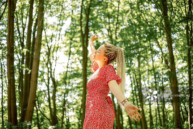 在森林里，举起手臂，穿着红色波点连衣裙，扎着辫子的有魅力的女人图片素材