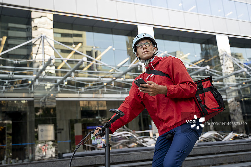 外卖员戴着自行车头盔和食品外卖包，在打电话，休息中图片素材