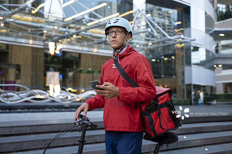 外卖员戴着自行车头盔和食品外卖包，在打电话，休息中图片素材