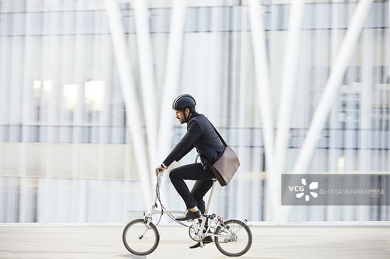 穿西装的商人骑自行车经过建筑物图片素材