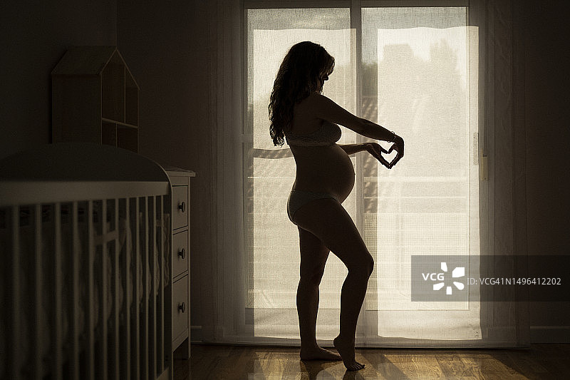 快乐的孕妇站在窗边图片素材