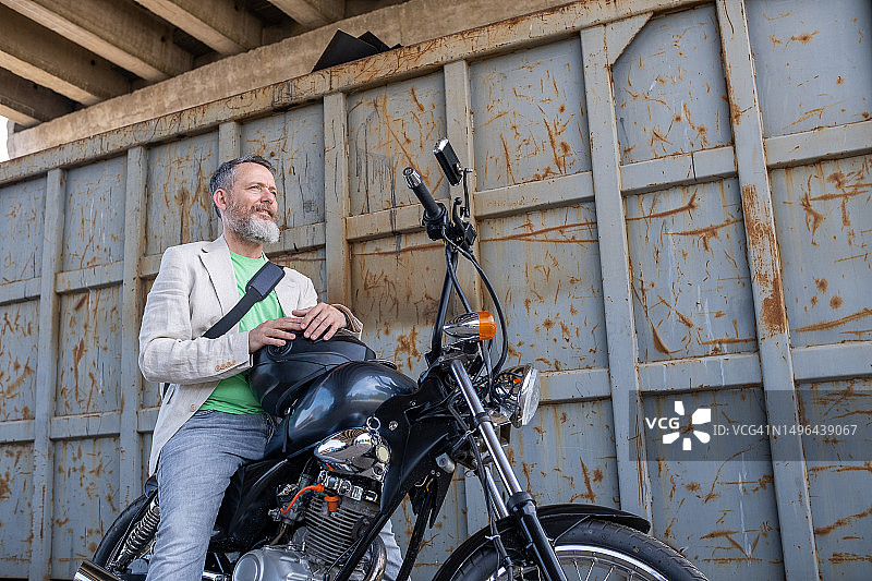 一位中年男人穿着浅绿色T恤、米色夹克和灰色牛仔裤，骑着一辆Bobber摩托车图片素材