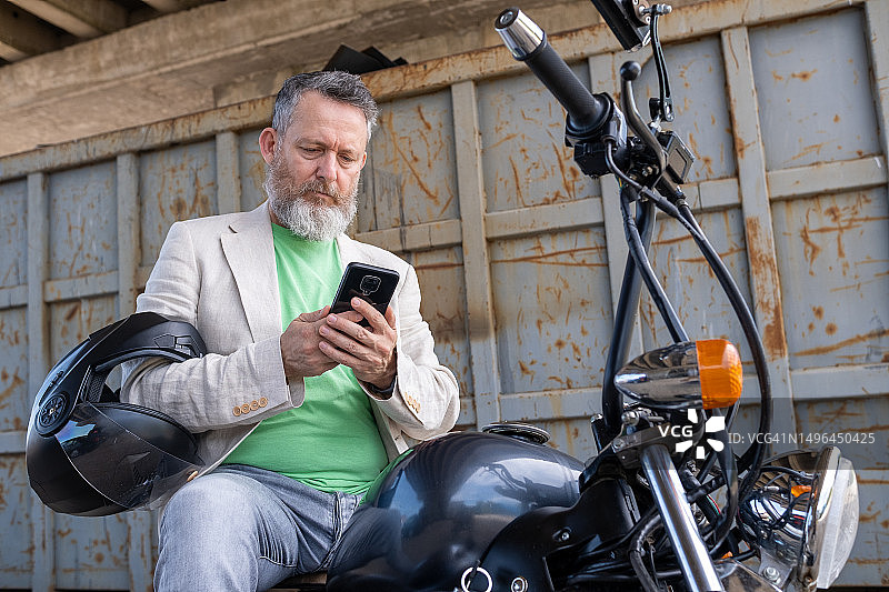 一位中年男人穿着浅绿色T恤、米色夹克和灰色牛仔裤，骑着一辆Bobber摩托车图片素材