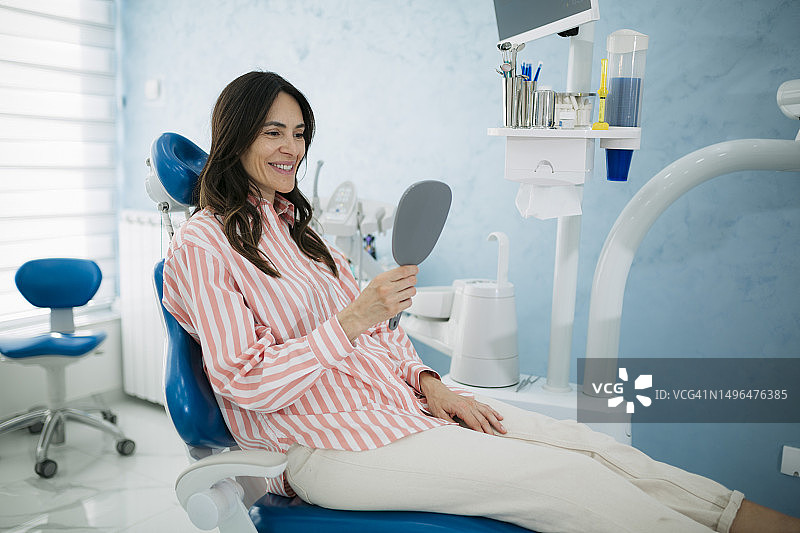 中年妇女在牙科诊所对着手持镜微笑图片素材
