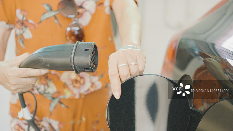 亚洲老年妇女在家插电为她的电动汽车充电，可持续的生活方式图片素材