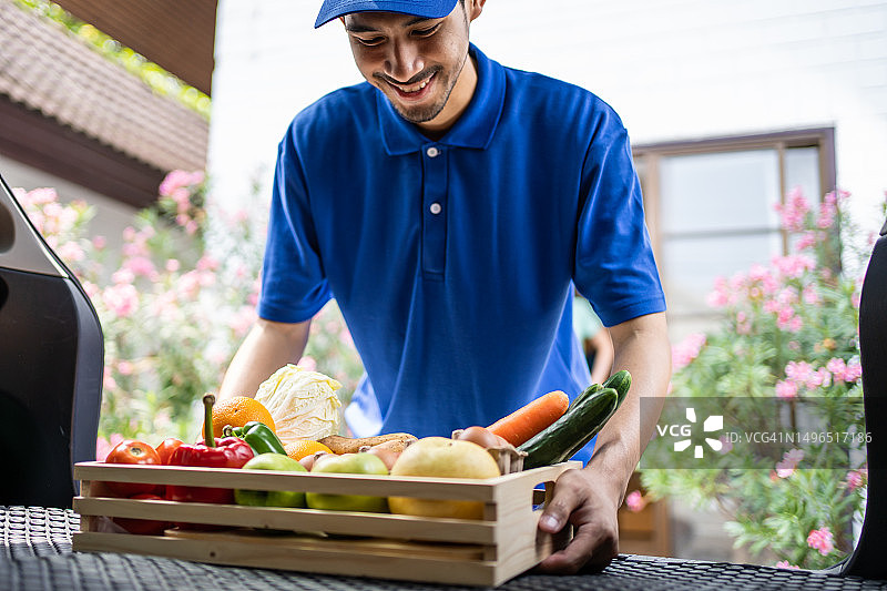 蓝色制服的亚洲男性送货员从车上搬运食品图片素材