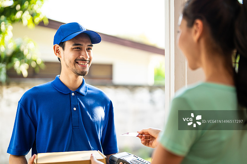 亚洲年轻快递员送货上门，女顾客信用卡支付图片素材
