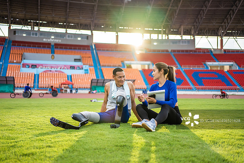装有假肢刀锋的亚洲残疾运动员和教练在体育场训练。有魅力的截肢男跑步运动员和女运动员在为残奥会跑步比赛练习后休息图片素材