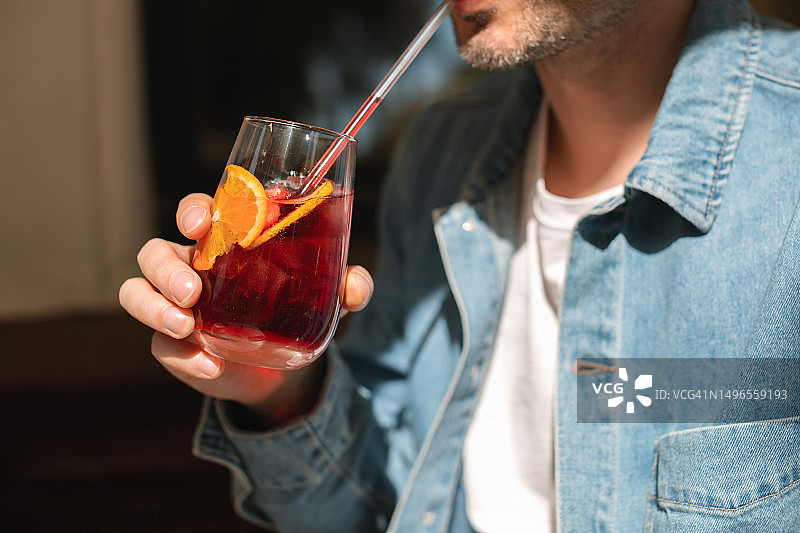 男人穿着牛仔夹克喝夏季鸡尾酒（含橙子片和草莓）特写图片素材