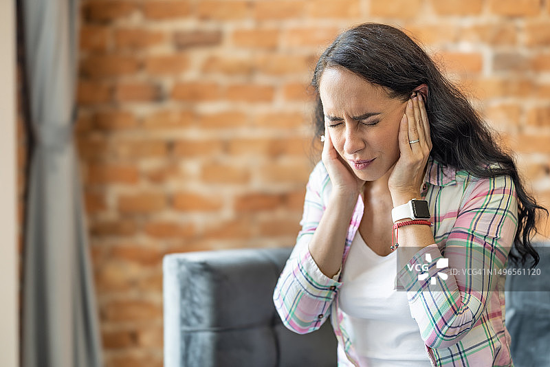 年轻女人头痛偏头痛，压力或耳鸣——耳朵里有噪音。一个女人患有严重的耳鸣，因疼痛而抓住头部的两侧。图片素材